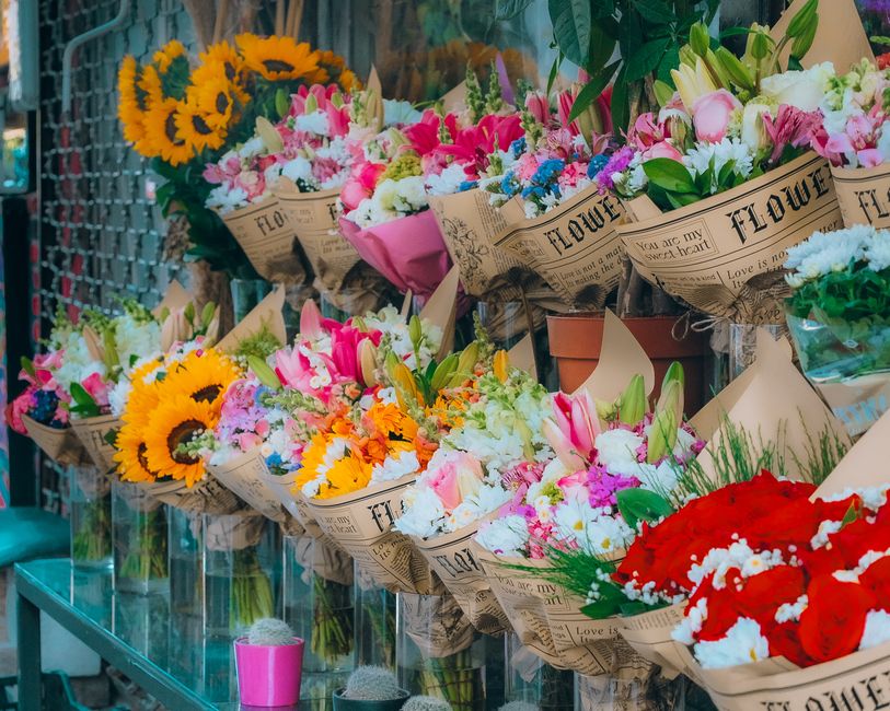 A display of vibrant flower bouquets arranged in brown paper wrapping with printed text, showcased in a florist shop. The bouquets feature a variety of fresh flowers, including bright yellow sunflower