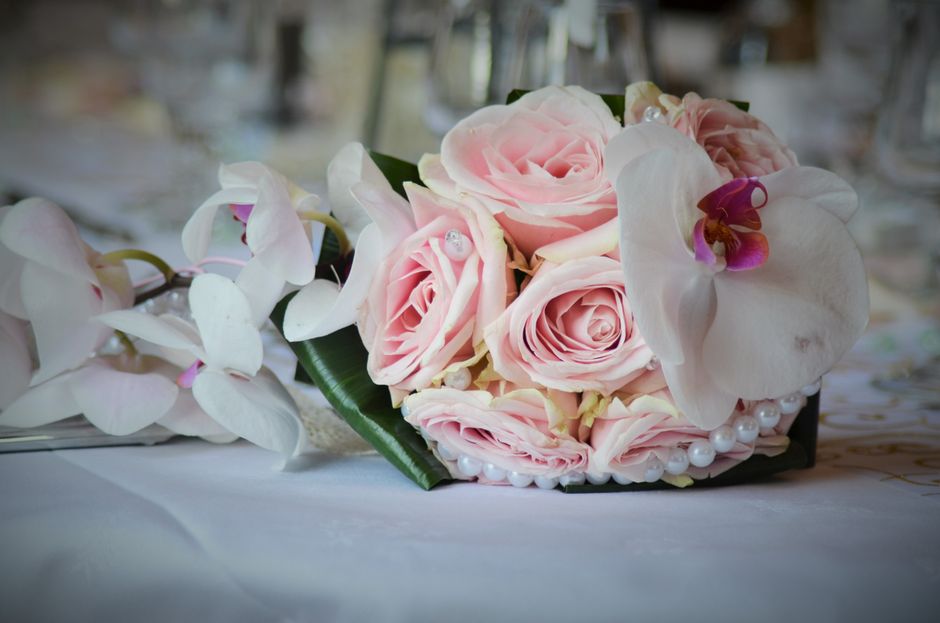 A floral arrangement featuring a bouquet of pale pink roses with tightly packed, velvety petals, complemented by white orchids with large, delicate petals and hints of purple at their centers. The bou